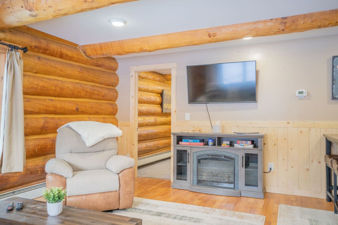 L’intérieur d’une cabane en rondins, avec une cheminée, un téléviseur fixé au mur et un coin salon confortable.