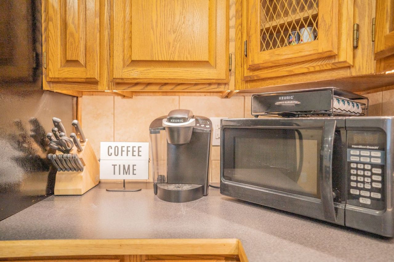 Una cocina con armarios de madera, cafetera, microondas y un letrero que dice 'COFFEE TIME'.