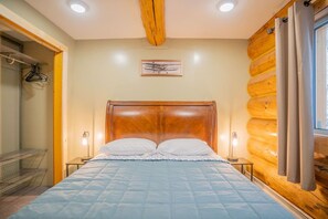 A bedroom with a wooden headboard, a bed with a blue quilt, bedside lamps, and a window with curtains.