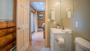 A bathroom with a wooden door, a sink with a mirror, and a toilet. - Tucked Away Timber Lower Suite (Fairbanks)
