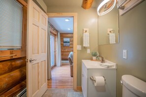 A bathroom with a wooden door, a sink with a mirror, and a toilet.