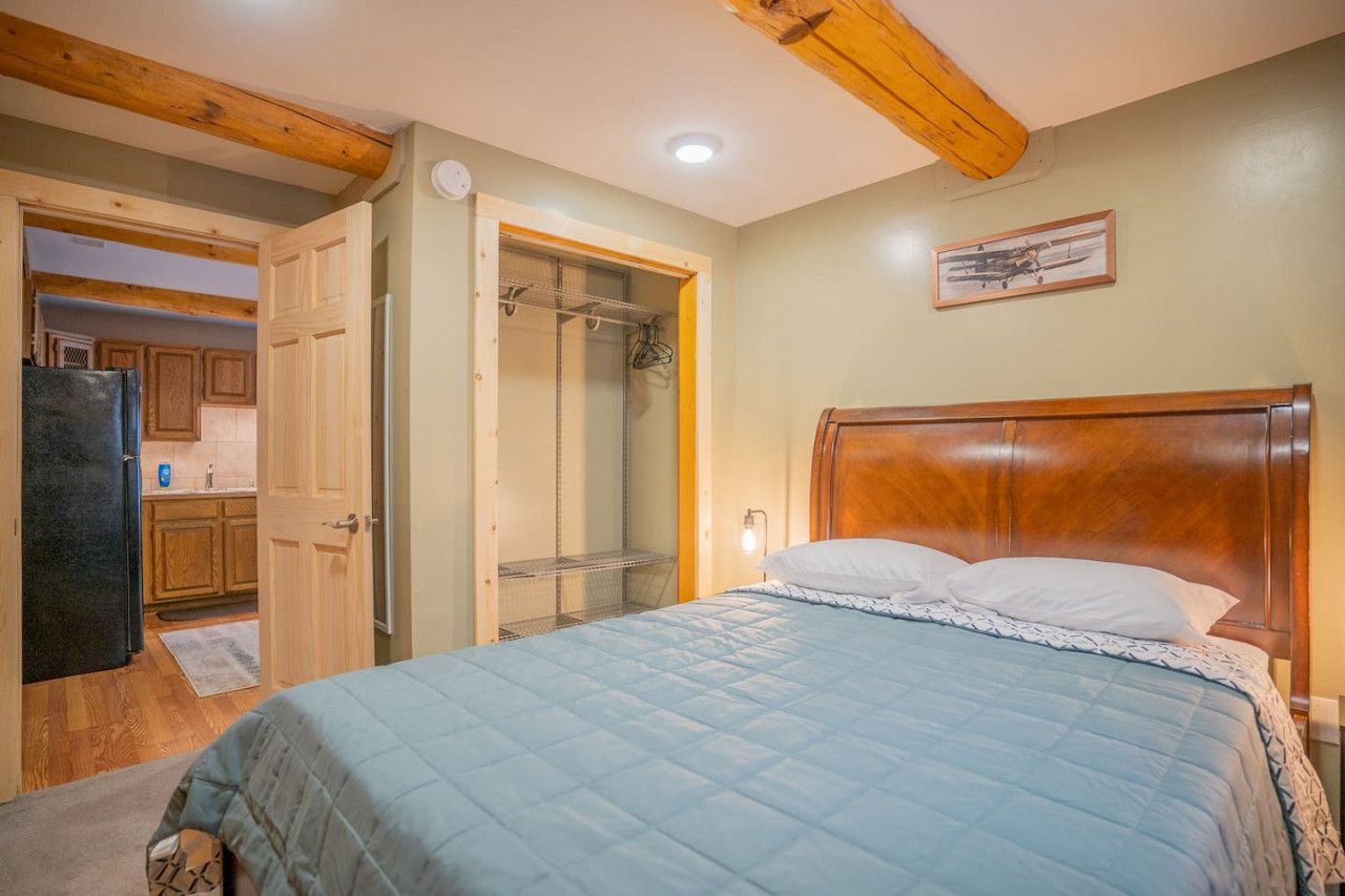 A bedroom with a wooden headboard, a bed with a blue quilt, a walk-in closet, and a shower.