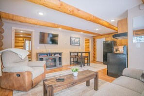 A log cabin interior with a living room, kitchen, and dining area.