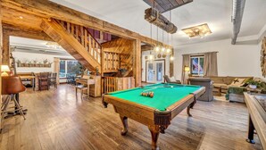 Amplia habitación con mesa de billar, suelo de madera, escalera y una zona de estar acogedora.