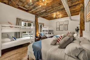 A room with bunk beds, a large bed, and a wooden ceiling.
