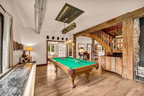 A spacious room with a pool table, wooden flooring, and a rustic staircase.