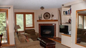 A living room with a fireplace, television, and a bookshelf. - Ski-in Ski-Out:King in Master; Quiet End Unit; high speed secure internet (Winter Park)