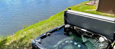 Un jacuzzi con panel de control, una mesa de patio y sillas, ubicado junto a un lago.