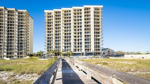 A wooden boardwalk leading to a beachfront hotel with multiple floors and balconies. - Escape to the Beach! Phoenix 8, 1402, 2 BR/2 Bath (Orange Beach)