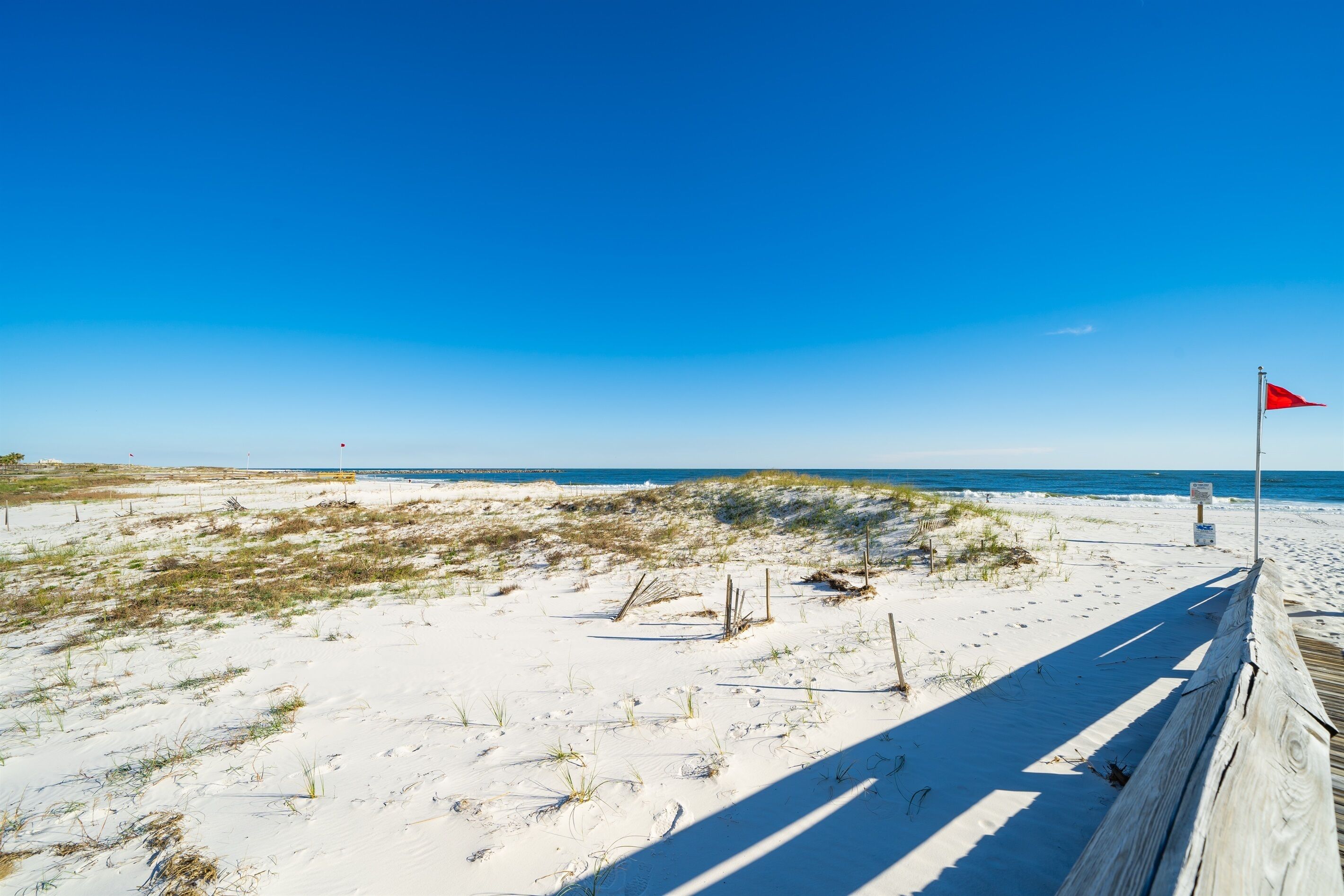 En sandstrand med en träpromenad och en röd flagga.