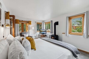 A modern hotel room with a large bed, a television, a fireplace, and multiple windows offering views of the outdoors.