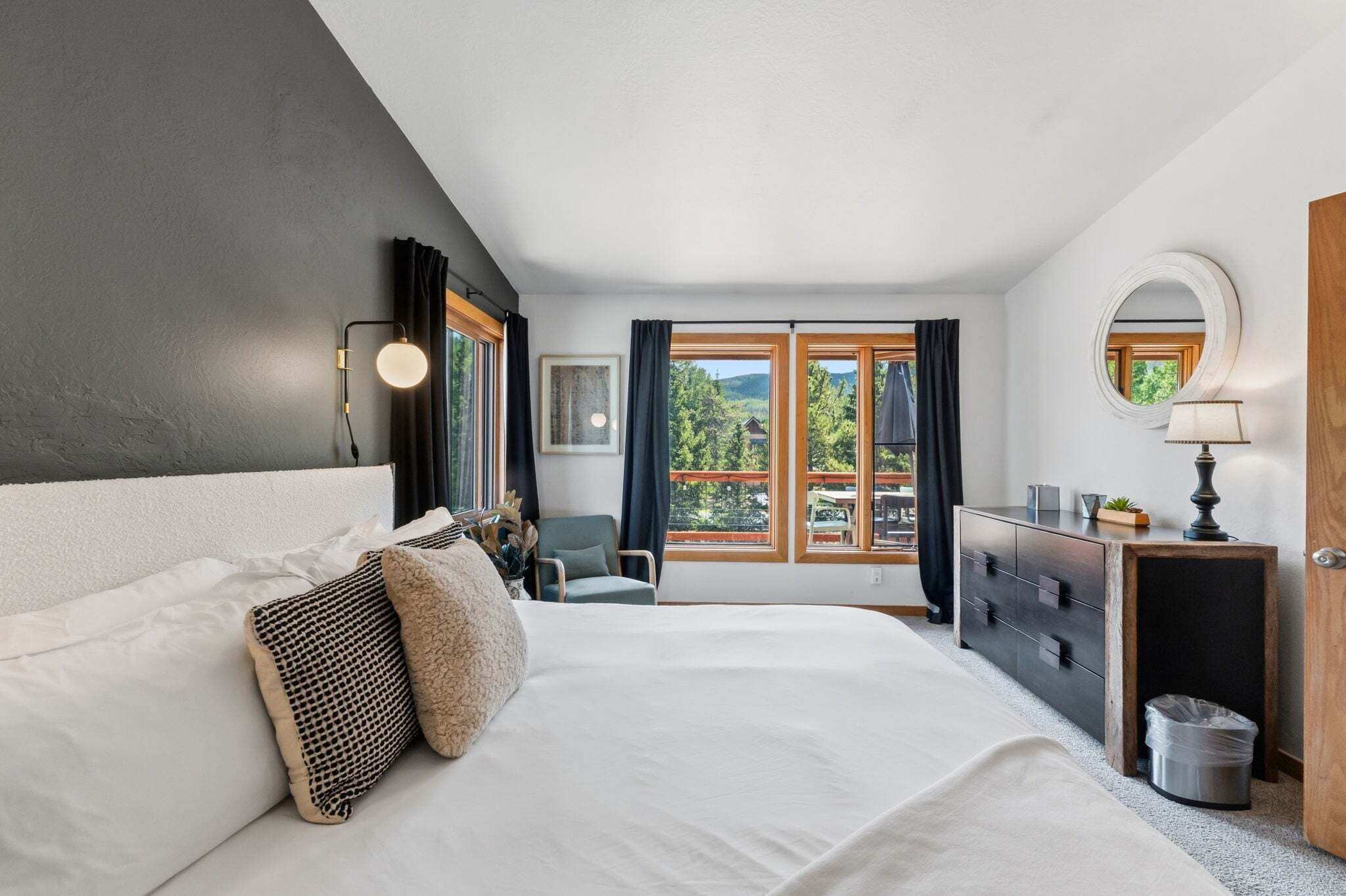 A bedroom with a large bed, a dresser, a chair, and a window with a view of greenery.