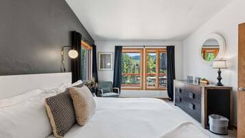 A bedroom with a large bed, a dresser, a chair, and a window with a view of greenery.