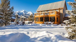 Eine Holzhütte mit Balkon, umgeben von schneebedeckten Bäumen und Bergen im Hintergrund.