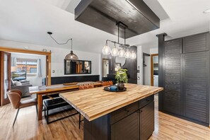 Une cuisine moderne avec un îlot central en bois, des luminaires suspendus et un grand miroir.