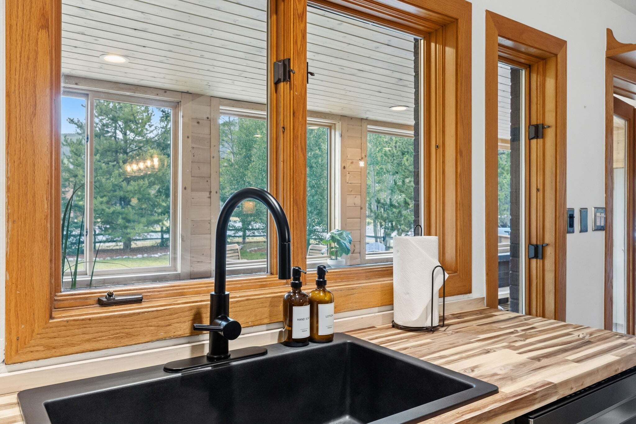 A modern kitchen with a black sink, wooden cabinetry, and large windows.
