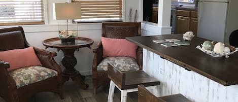 A kitchen with wooden cabinets, a refrigerator, and a dining area with a bar stool and two chairs.