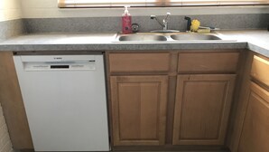 A kitchen with a Bosch dishwasher, wooden cabinets, a double sink, and a doormat with the text "LIFE'S BETTER on the BEACH".