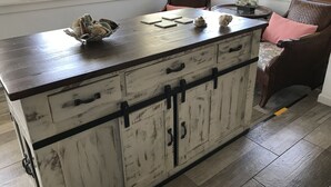 A rustic wooden cabinet with drawers and a countertop, placed in a room with a chair and a lamp.