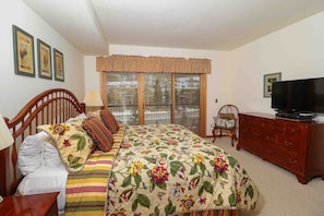 Quarto com cama, penteadeira, televisão e janela com persianas.