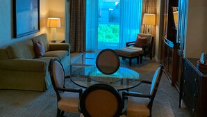 Ein Hotelzimmer mit einem Glastisch, zwei Sofas, einem Fernseher und einem großen Fenster mit Vorhängen.