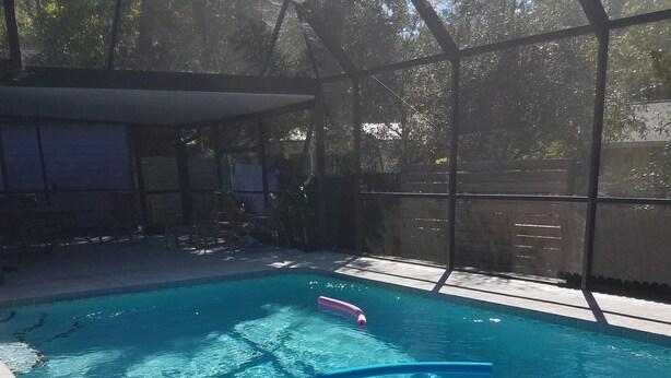 Piscina transparente com boia rosa, rodeada por área coberta com cadeiras e cerca de madeira.