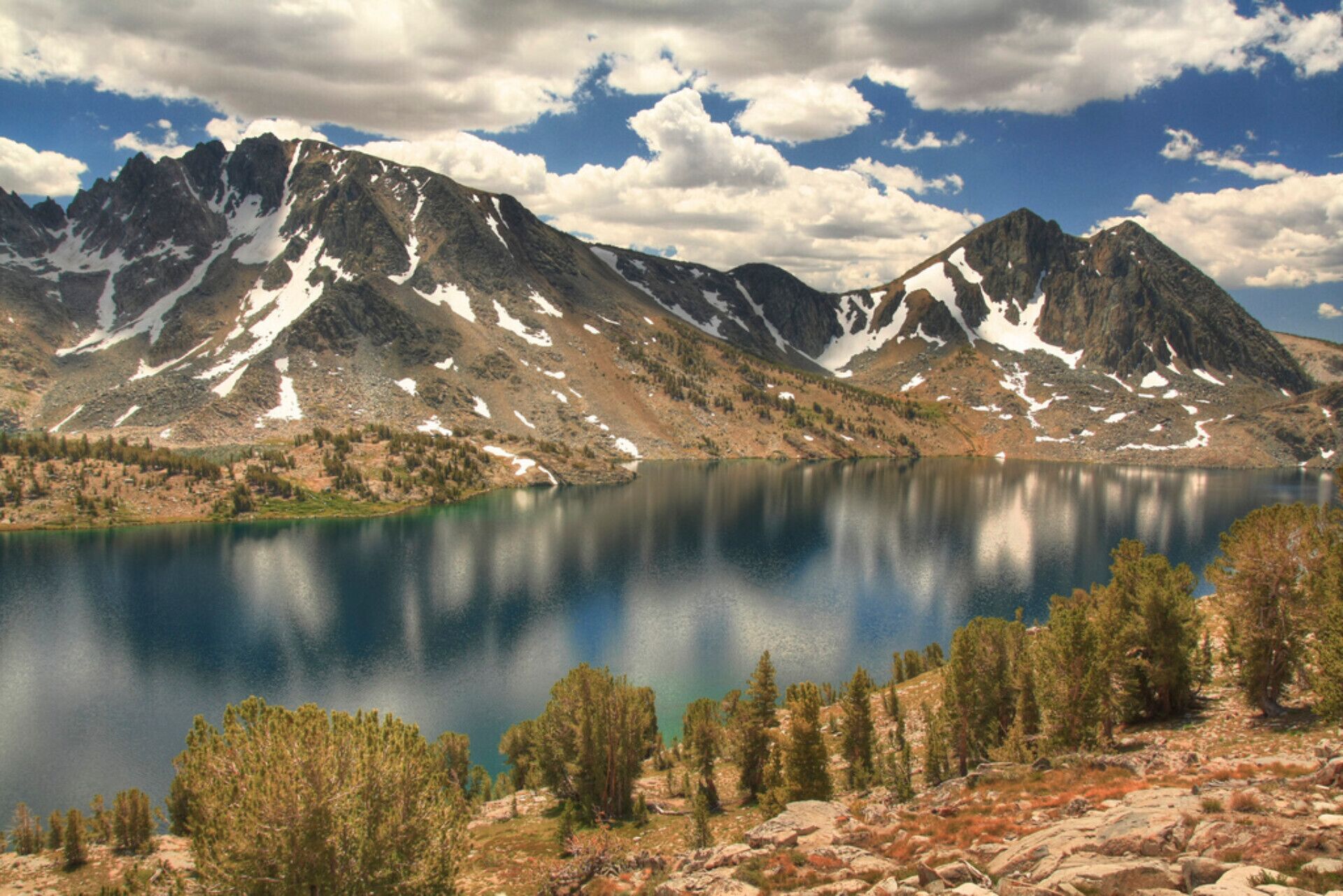 Paisatge de muntanyes amb un llac, arbres i terreny rocos.