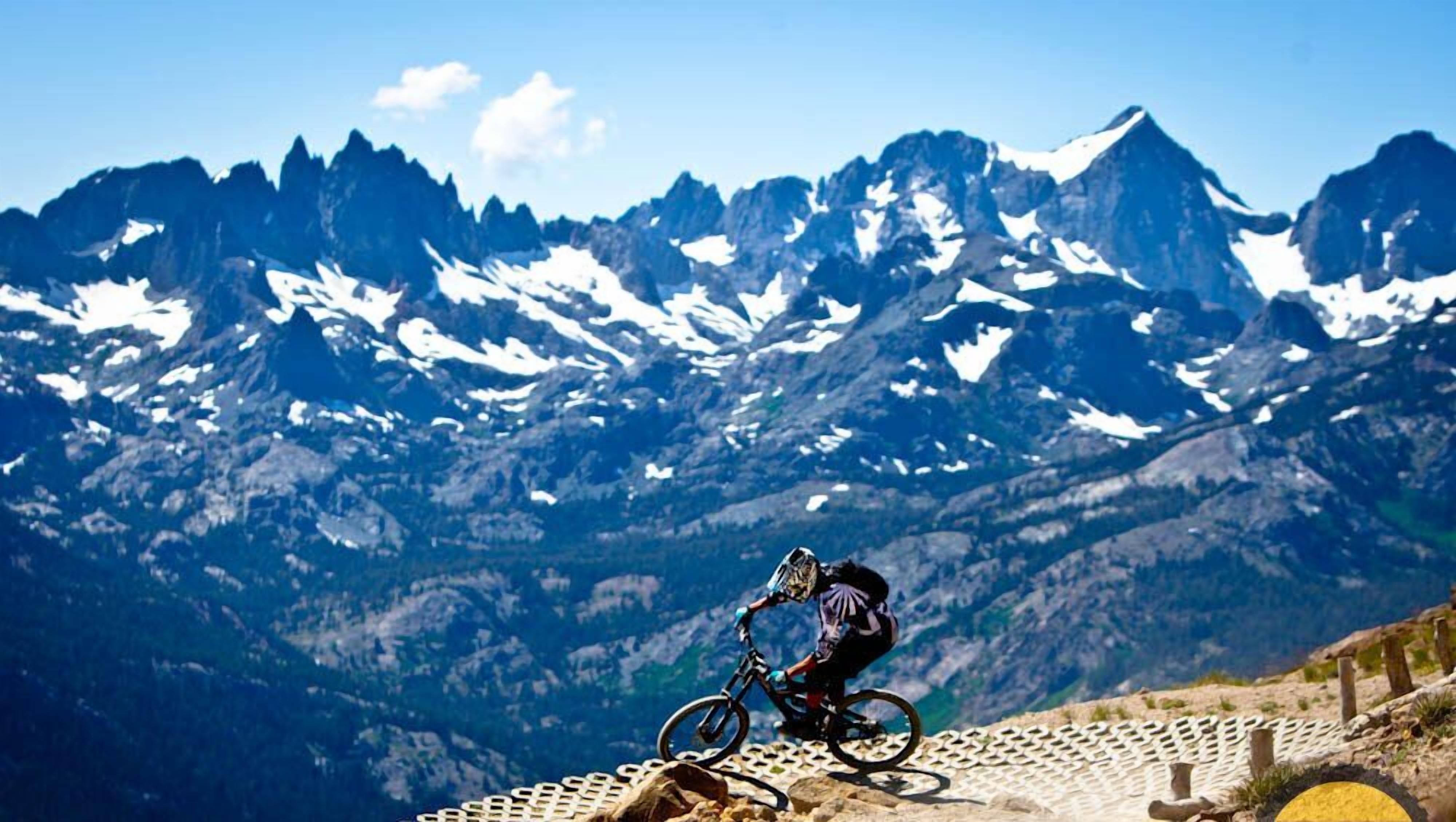 A mountain biker on a trail with a scenic mountain backdrop.
