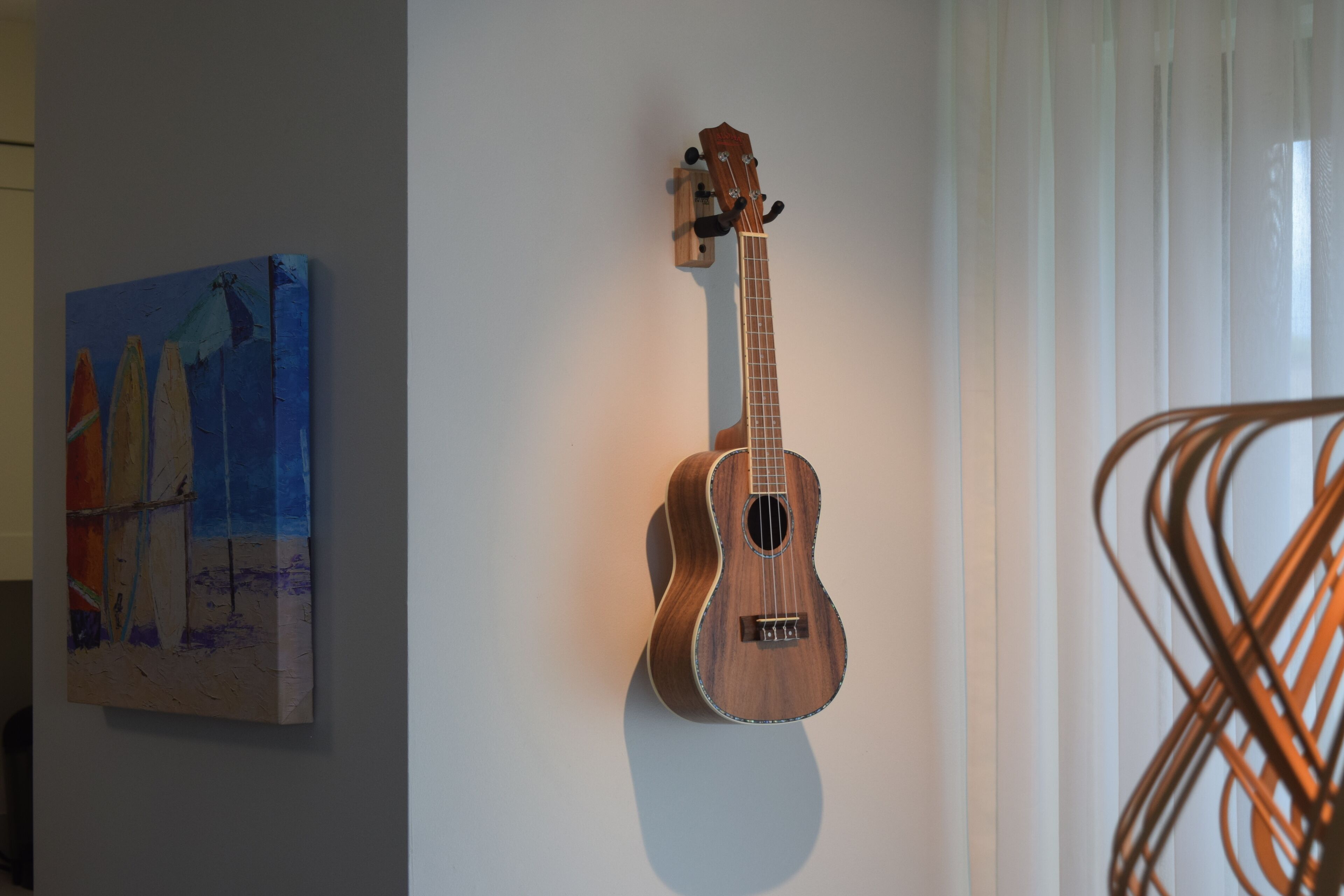 Un ukulélé accroché au mur, un tableau et une chaise.