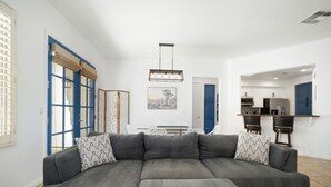 A modern living room with a sectional sofa, a dining table, and a kitchen area. - Legacy Villas private villa w/ view- steps to pool- bikes & arcade game included (La Quinta)