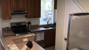 Una cocina con encimeras de granito, estufa, pileta, alacenas de madera y ventana con persianas.
