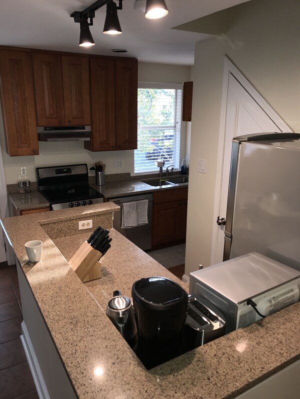 A kitchen with granite countertops, a stove, a sink, wooden cabinets, and a window with blinds.