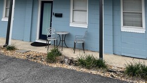 Un motel de dos pisos con fachada azul, un balcón en el segundo piso y un pequeño espacio al aire libre con sillas y una mesa de metal.