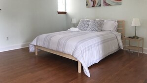 Un dormitorio con una cama de madera, ropa de cama blanca, dos lámparas de noche y una obra de arte abstracta en la pared.