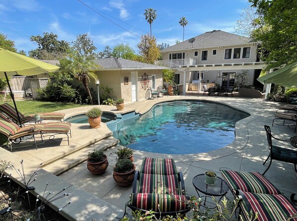 A backyard with a swimming pool, lounge chairs, and potted plants.