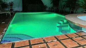 A swimming pool with a green-lit edge, surrounded by lounge chairs and a tiled deck. - Private home with pool and only a block to the beach, restaurants, nightlife... (Jaco Beach)