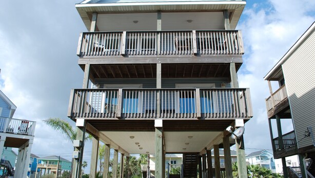A multi-story building with balconies, a central staircase, and a blue roof. - Sunny Beach Luxurious House with View, Sleeps 12, Steps From Beach (Galveston)