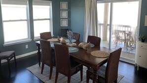 A dining room with a dark wooden table, wicker chairs, and a hanging light fixture. - Sunny Beach Luxurious House with View, Sleeps 12, Steps From Beach (Galveston)