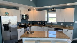 A modern kitchen with white cabinets, stainless steel appliances, a granite countertop, and a sign indicating a beach direction. - Sunny Beach Luxurious House with View, Sleeps 12, Steps From Beach (Galveston)