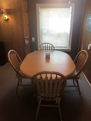 Una mesa de madera con cuatro sillas, un extintor y una ventana con persianas.