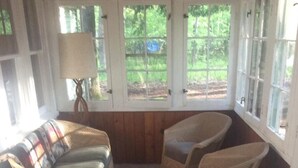 Un cuarto acogedor con un sofá, dos sillones y un sillón estampado. Amplias ventanas con vistas a zonas verdes.