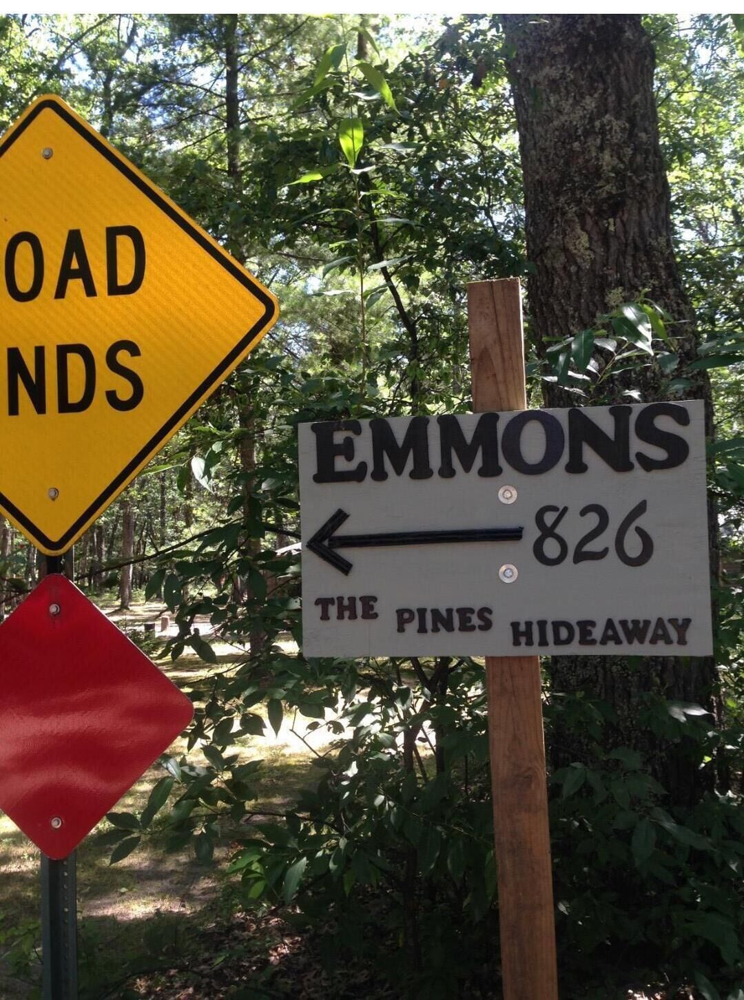 A directional sign for 'EMMONS 826 THE PINES HIDEAWAY' with a yellow diamond-shaped sign indicating 'ROAD NDS' nearby.