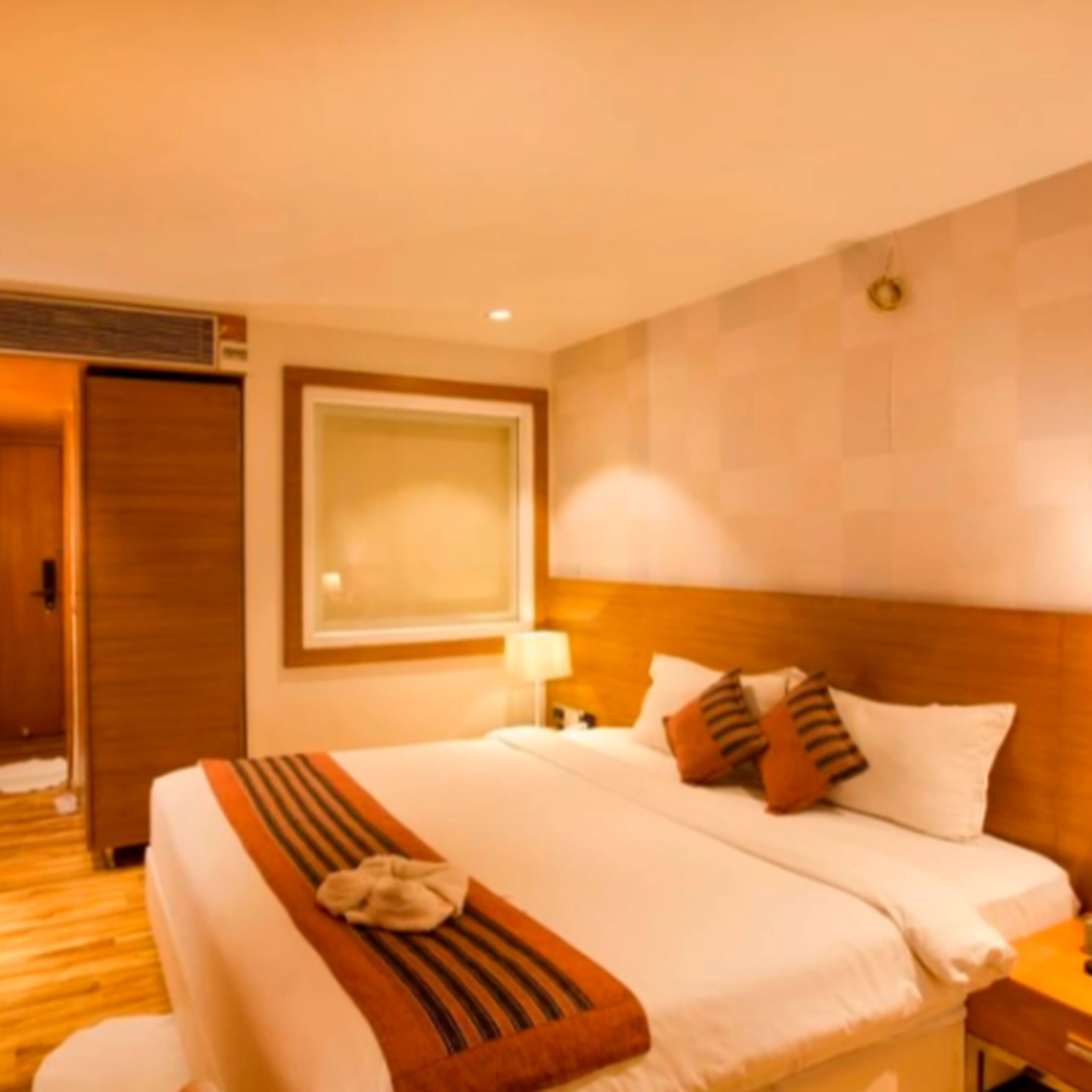 A hotel room with a bed, a bedside table, a lamp, and a wall-mounted picture frame.