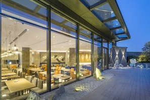 A modern restaurant with a glass facade, outdoor seating, and a stone sculpture. - Holiday Inn Express Suzhou New District by IHG (Suzhou)