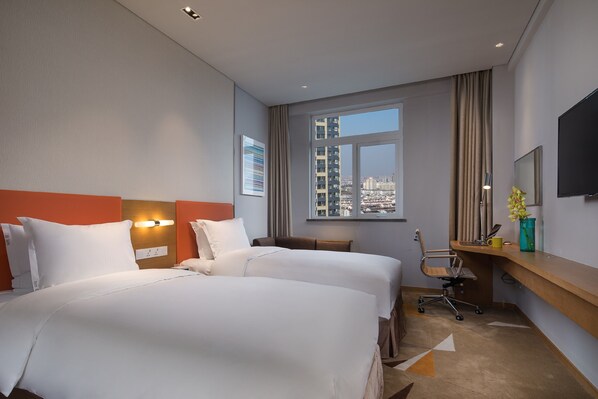 Une chambre d’hôtel avec deux lits, un bureau, une chaise, une télévision et une fenêtre donnant sur la ville.
