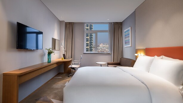 A hotel room with a large bed, a desk with a flat-screen TV, a small table, and a window with a city view. - Holiday Inn Express Suzhou New District by IHG (Suzhou)