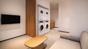 A modern laundry room with a flat-screen TV mounted on the wall, a bench, and a sofa. - Holiday Inn Express Suzhou New District by IHG (Suzhou)