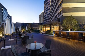 Un espace extérieur aménagé en terrasse, avec des tables et des chaises, entouré d’immeubles.