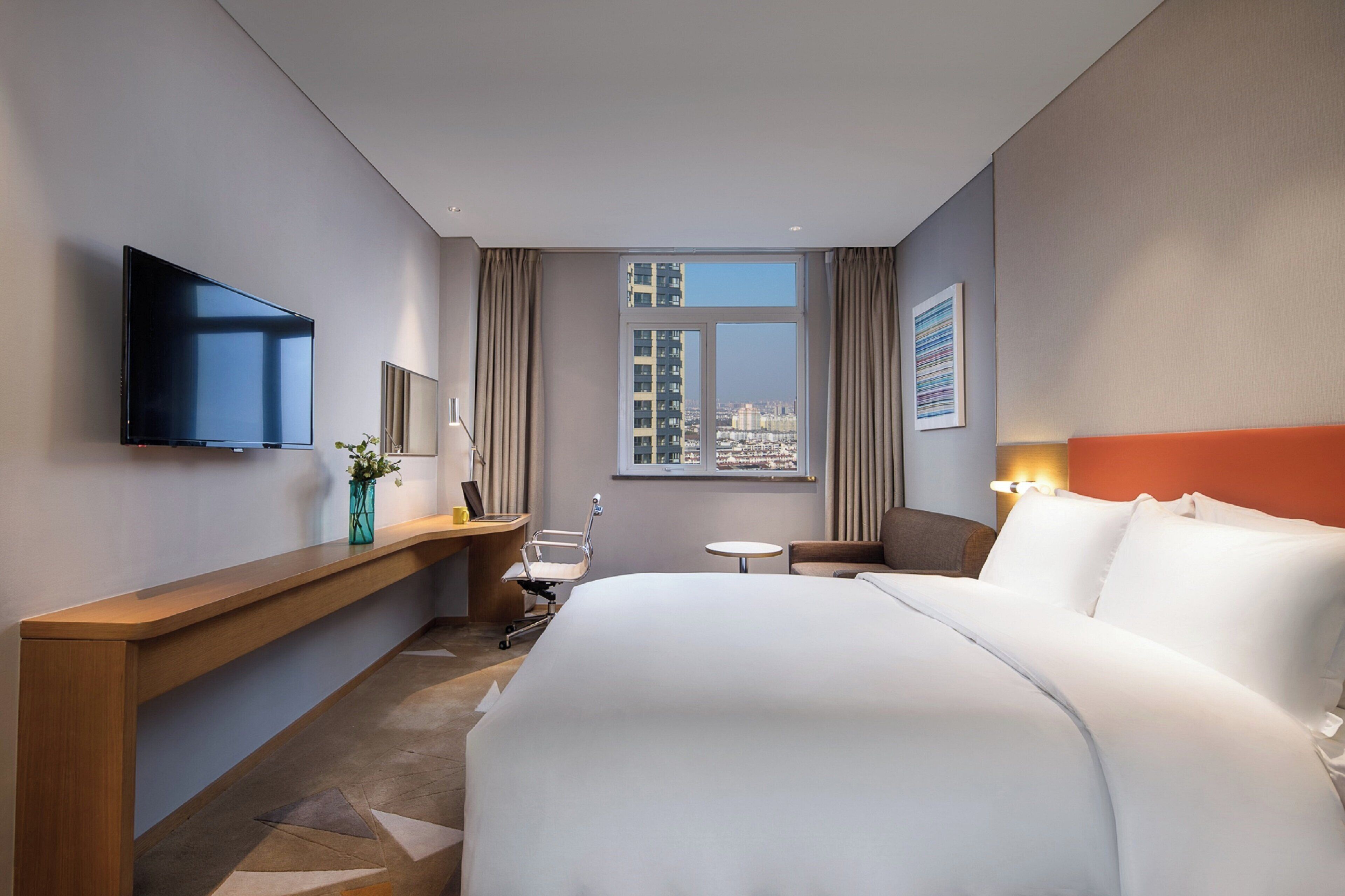 Habitación de hotel con una cama grande, un escritorio con silla, televisión, ventana con vista a la ciudad y una mesita.