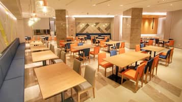 A spacious dining area with multiple tables and chairs, a long bench along one wall, and a modern chandelier.